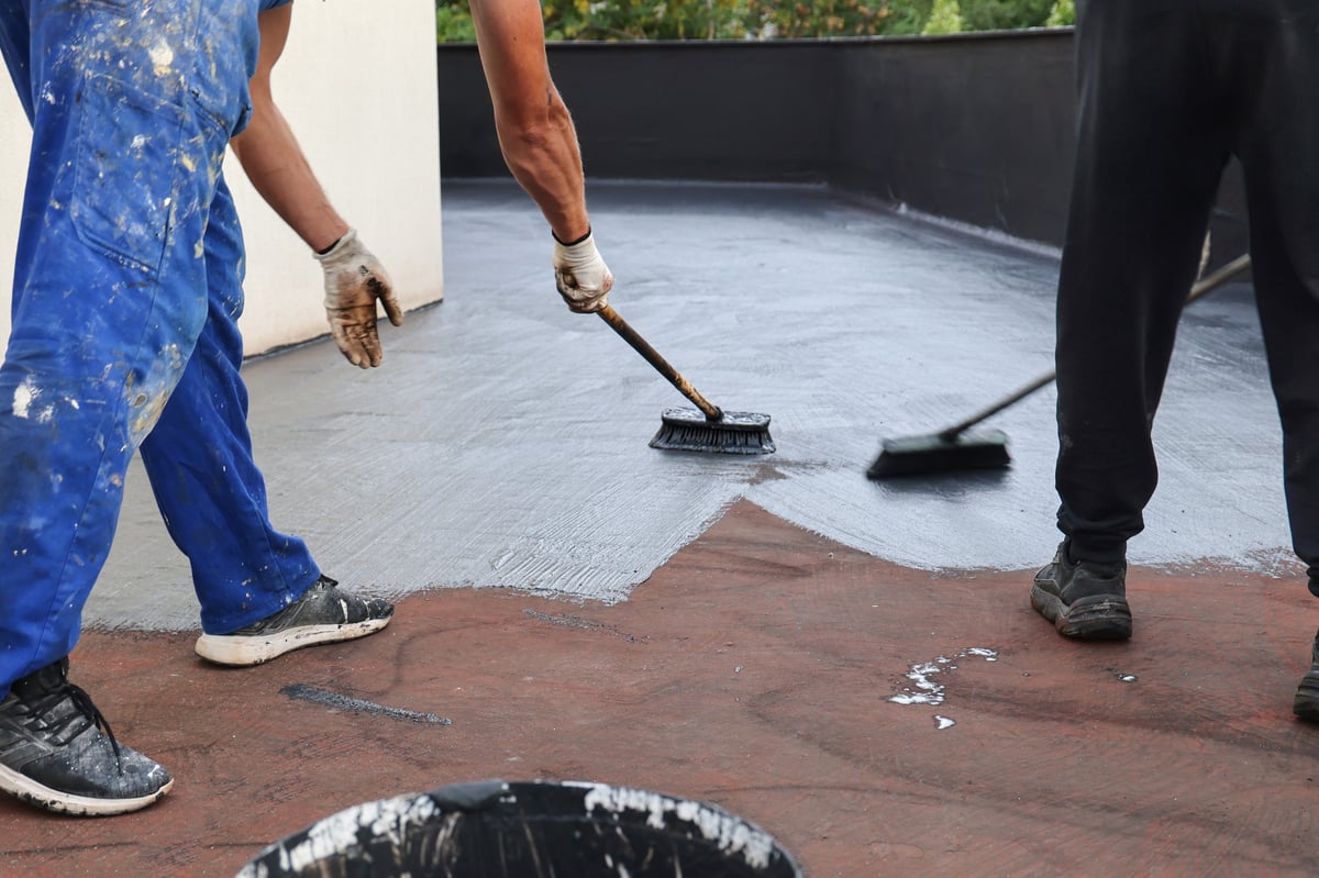 Workers applying waterproofing coating on building roof