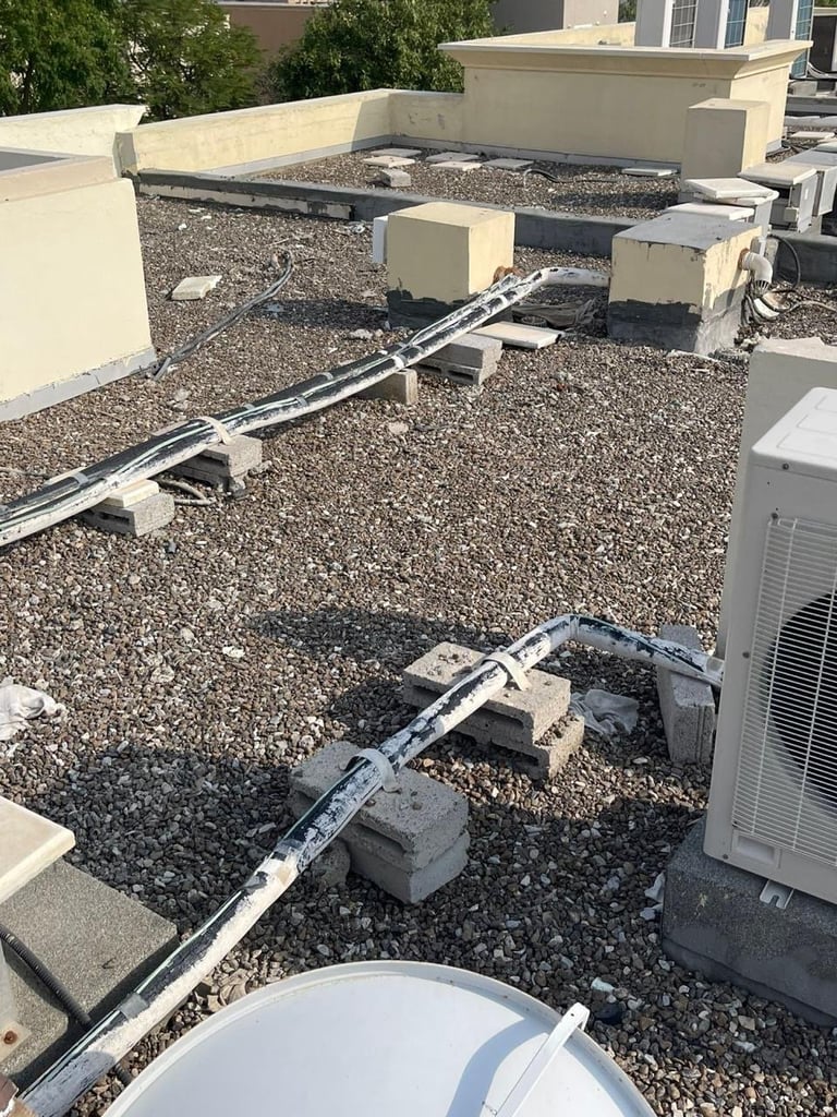 Flat commercial rooftop with gravel, HVAC units, concrete parapets, and white conduit piping