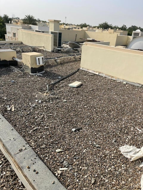 Flat rooftop with gravel, beige walls, and mechanical equipment in an urban area with palm trees visible